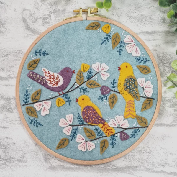 Three beautiful embroidered birds against a pale blue felt background, mounted in an embroidery hoop.